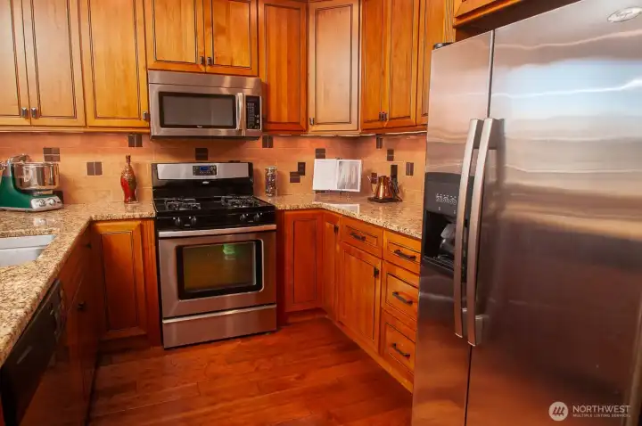 Open kitchen has slab granite countertops, double sink, gas range, extensive strorage, and double-door refrigerator.