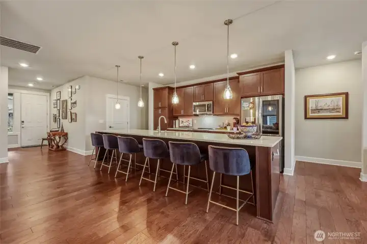 Den/Office is to the right of the door to the garage showing in this photo.  LOVE the huge island & GROOVY pennant lighting.  Upgrades included Over & Under Cabinet Lighting controlled by remote and an app.  Primary bedroom to the right.