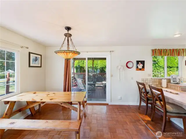 Dining area is graced by the stained glass fixtures and the parquet flooring.  Note sit-down eating area in kitchen.  Slider to covered patio.  Photo a bit stretched by wide-angle lens.