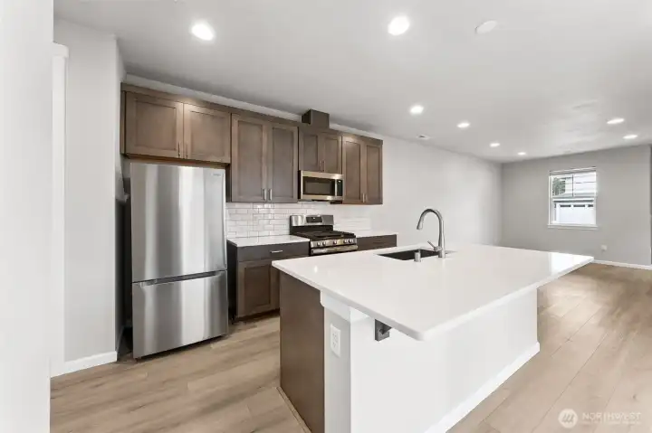 Open kitchen to living room area- quartz countertops, stainless steel appliances, gas stove, subway tile backsplash, LVP flooring + pantry.