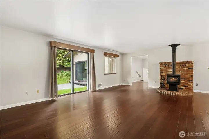Livingroom with a wood burning fireplace and slider to the backyard. Just beyond the fireplace is the den/office space, primary bedroom to the left and straight ahead to the shop.
