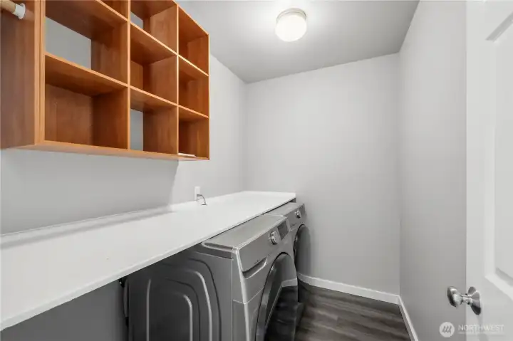 Spacious laundry area with washer and dryer included, built-in shelving, and room to fold laundry