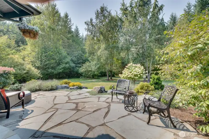 The gorgeous stone patio is an inviting outdoor retreat, perfect for relaxing or entertaining, and seamlessly blends elegance with durability, providing a charming space for dining, lounging, or enjoying the surrounding landscape. Surrounded by lush landscaping and open views of the acreage, this patio creates a serene extension of the home’s indoor living spaces.
