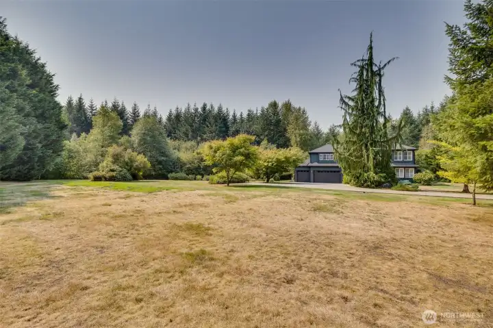 Expansive open acreage stretches toward the home.  Rolling lawns, mature trees, including fruit trees, and natural landscaping provide a picturesque backdrop, framing the house beautifully from every angle. This vast outdoor area offers endless possibilities for recreation, gardening, or simply enjoying the serenity of country living, while enhancing the property’s elegant and welcoming presence.  Horses are welcome, too!