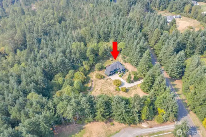From this soaring drone perspective, the full scope of the property comes into view. The elegant home sits gracefully amidst 5.74 acres of lush, private acreage, with the winding driveway, stone patio, and surrounding landscaping all visible. This vantage point captures the home’s impressive scale, sophisticated design, and serene setting within the gated community, highlighting both its beauty and the expansive natural surroundings.