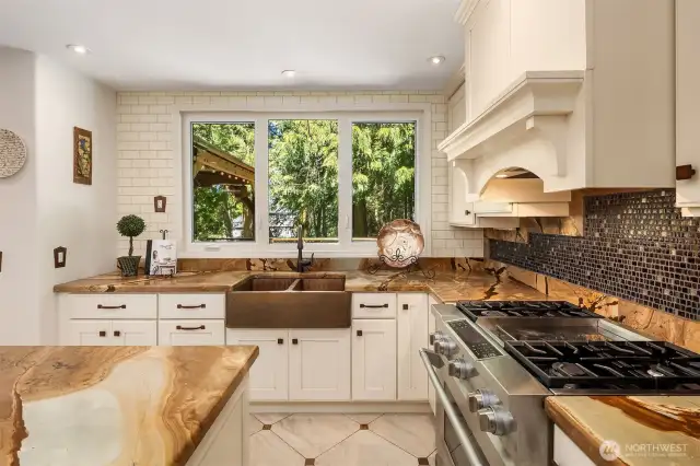 Rustic charm meets elegance in this open-concept kitchen with stone countertops, copper sink, and tree-lined views.