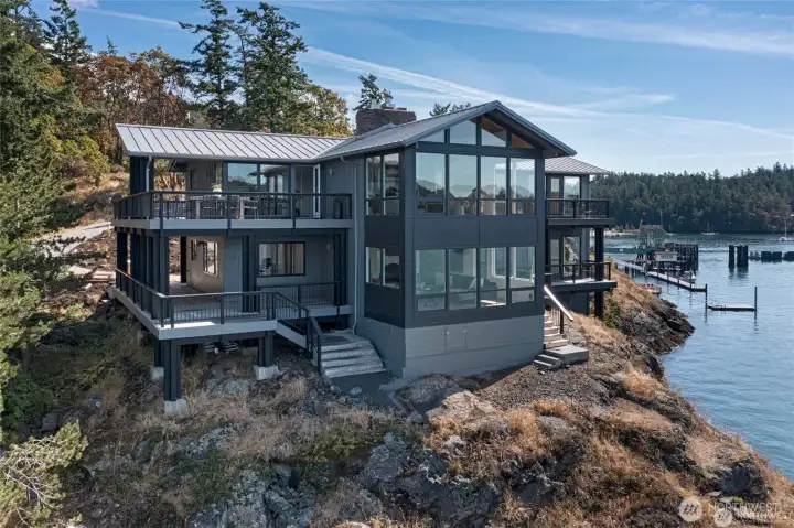 A striking water-level perspective reveals the home’s modern multi-level architecture with walls of glass, wraparound decks, and breathtaking views toward Blind Bay and the ferry landing.