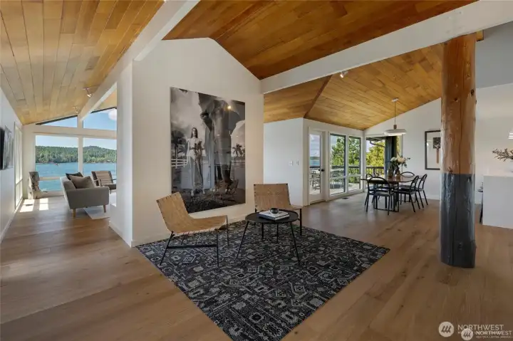 This formal living space features vaulted ceilings, floor-to-ceiling windows, and warm wood finishes, capturing uninterrupted views across the channel and filling the home with natural light.