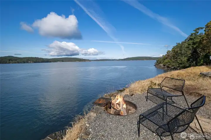 A wider angle showcases the firepit area overlooking miles of pristine Orcas Island waterfront, with serene west-facing views and natural rocky shoreline creating a peaceful retreat.