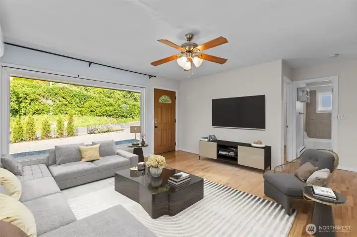 Virtually staged living room highlighting the home’s open feel, oversized picture window, hardwood floors and abundant natural light throughout.