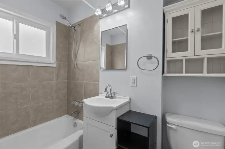 Full bathroom featuring updated tile surround, natural light and functional built-in storage.