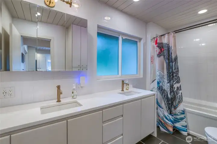 Updated upstairs full bathroom with dual-sink quartz vanity, modern fixtures, radiant in-floor heat, smart toilet, tile flooring, and tub/shower combination.