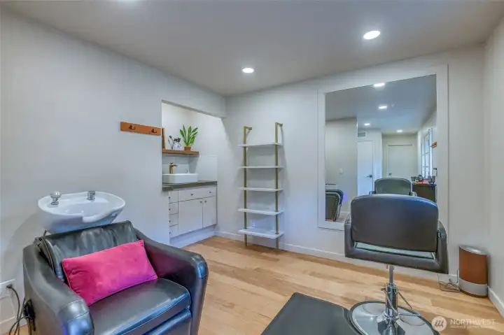 Main-level flex studio with sink, built-in shelving, and large wall mirror. Chairs shown will be removed. Ideal for a home office, creative studio, or hobby room.