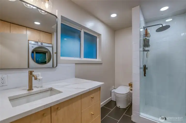 Stylish downstairs 3/4 bath with quartz vanity, smart toilet, glass-enclosed shower, radiant heated floors, built-in storage, and thoughtfully integrated laundry.