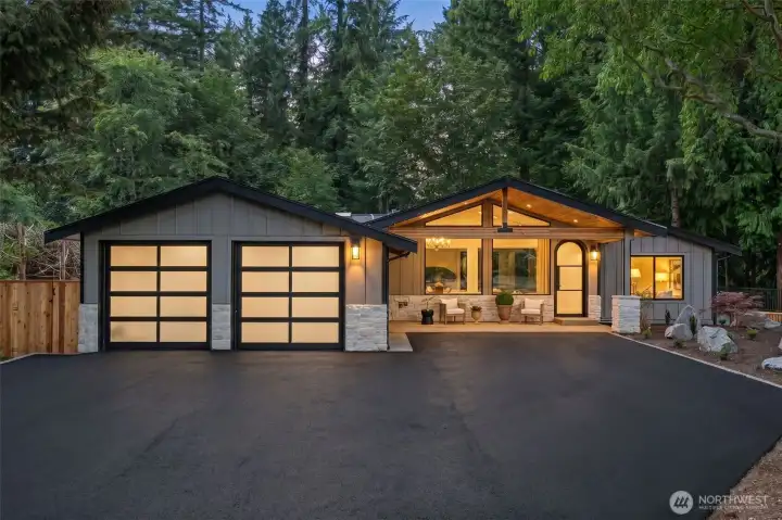 Dramatic vaulted timber-frame architecture sets a striking first impression, with a soaring wood-lined portico, stacked stone accents, and dual glass-panel garage doors framed against towering evergreens. A freshly landscaped entry with boulder accents and a covered lounge area invites gracious, one-level living from the moment you arrive. Dramatic vaulted timber-frame architecture sets a striking first impression, with a soaring wood-lined portico, stacked stone accents, and dual glass-panel garage doors framed against towering evergreens. A freshly landscaped entry with boulder accents and a covered lounge area invites gracious, one-level living from the moment you arrive.