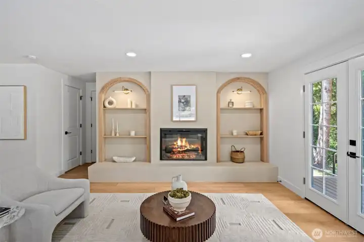 The great room's arched built-in feature wall anchors the space, framing a sleek eletric fireplace between custom wood archways and floating display shelves. Wide-plank engineered hardwood flows underfoot, while French doors just beyond invite effortless indoor-outdoor living. The great room's arched built-in feature wall anchors the space, framing a sleek eletric fireplace between custom wood archways and floating display shelves. Wide-plank engineered hardwood flows underfoot, while French doors just beyond invite effortless indoor-outdoor living.