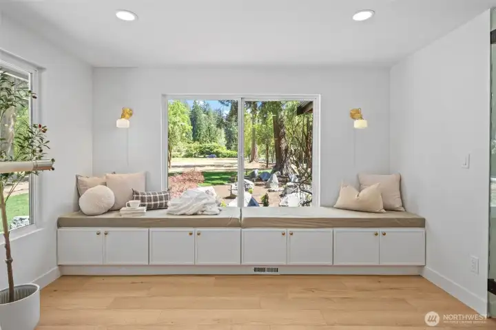 A built-in window seat with concealed cabinet storage below, framed by brass sconces and a picture window overlooking the landscaped grounds. Wide-plank engineered hardwood and abundant natural light make this a versatile spot for quiet mornings or a favorite reading nook. A built-in window seat with concealed cabinet storage below, framed by brass sconces and a picture window overlooking the landscaped grounds. Wide-plank engineered hardwood and abundant natural light make this a versatile spot for quiet mornings or a favorite reading nook.