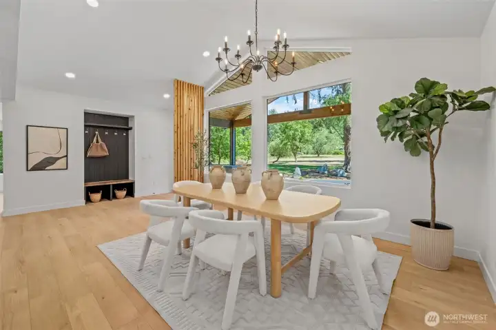 Vaulted ceilings and a wood-lined gable peak soar above this dining space, framed by oversized picture windows that fill the room with natural light and greenery views. A cedar slat accent wall adds architectural texture, while wide-plank engineered hardwood carries the space into the adjoining nook for effortless everyday flow. Vaulted ceilings and a wood-lined gable peak soar above this dining space, framed by oversized picture windows that fill the room with natural light and greenery views. A cedar slat accent wall adds architectural texture, while wide-plank engineered hardwood carries the space into the adjoining nook for effortless everyday flow.