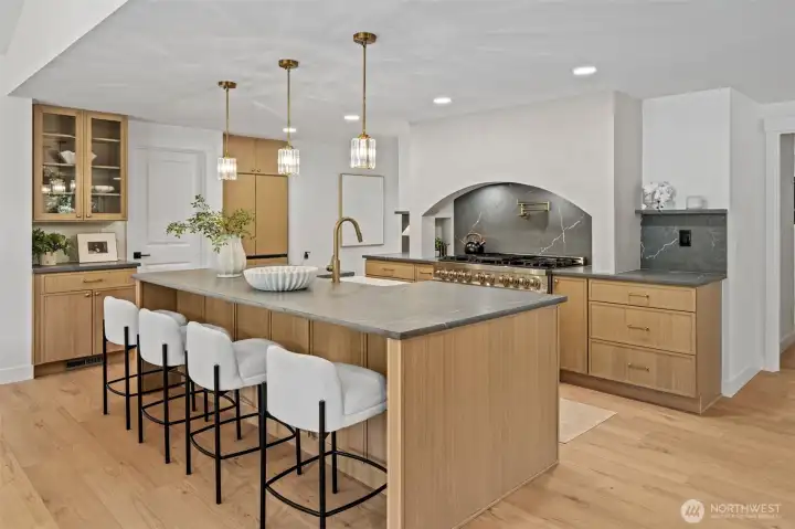 Custom oak cabinetry lines the perimeter, including glass-front display cabinets that add depth and character to the room. Brass hardware and fixtures tie the space together, while the open layout connects effortlessly to the adjoining dining and living areas. Custom oak cabinetry lines the perimeter, including glass-front display cabinets that add depth and character to the room. Brass hardware and fixtures tie the space together, while the open layout connects effortlessly to the adjoining dining and living areas.