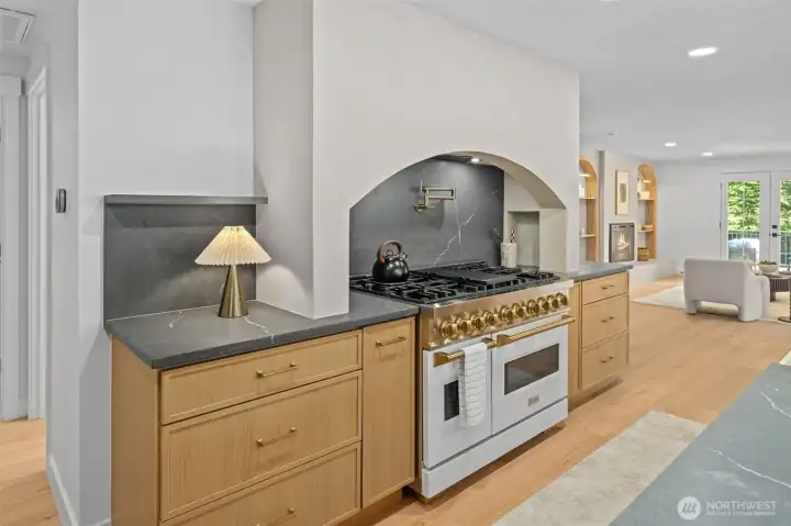 This home introduces a Zeline professional-style range framed by an arched stone surround and pot filler. Honed stone counters and custom oak cabinetry complete the striking backdrop. Notice the shelfing on the sides for additional decor. This home introduces a Zeline professional-style range framed by an arched stone surround and pot filler. Honed stone counters and custom oak cabinetry complete the striking backdrop. Notice the shelfing on the sides for additional decor.