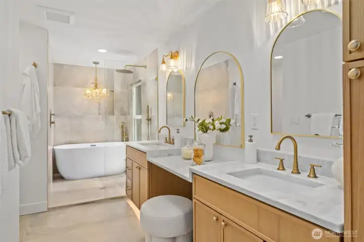 Arched brass-framed mirrors and dual vanities set an elevated tone in this spa-inspired ensuite, complemented by marble-look quartz counters and warm brass fixtures throughout. A glass-enclosed walk-in shower and freestanding soaking tub, illuminated by a crystal chandelier, complete this serene retreat. Arched brass-framed mirrors and dual vanities set an elevated tone in this spa-inspired ensuite, complemented by marble-look quartz counters and warm brass fixtures throughout. A glass-enclosed walk-in shower and freestanding soaking tub, illuminated by a crystal chandelier, complete this serene retreat.