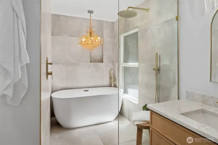 The freestanding soaking tub sits framed by large-format tile and a picture window, with a glass-enclosed rain shower just beyond. Overhead, a crystal chandelier adds a touch of drama to this quiet corner of the ensuite. The freestanding soaking tub sits framed by large-format tile and a picture window, with a glass-enclosed rain shower just beyond. Overhead, a crystal chandelier adds a touch of drama to this quiet corner of the ensuite.