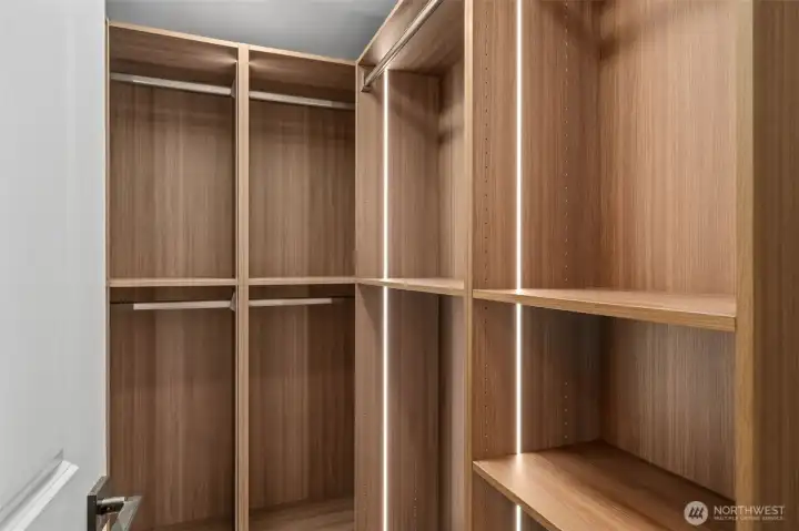 Custom walnut-toned built-ins line this walk-in closet, complete with integrated LED lighting and multiple hanging rods for organized, everyday storage. Adjustable shelving throughout offers flexible space to keep every wardrobe need in its place. Custom walnut-toned built-ins line this walk-in closet, complete with integrated LED lighting and multiple hanging rods for organized, everyday storage. Adjustable shelving throughout offers flexible space to keep every wardrobe need in its place.