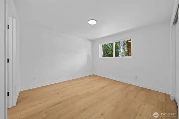 Bedroom Three features a window overlooking mature trees, filling the room with natural light throughout the day. Fresh paint and wide-plank engineered hardwood create a blank canvas, ready for a guest room, home office, or creative space. Bedroom Three features a window overlooking mature trees, filling the room with natural light throughout the day. Fresh paint and wide-plank engineered hardwood create a blank canvas, ready for a guest room, home office, or creative space.