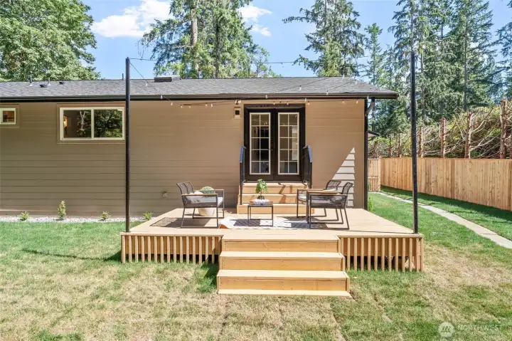 Just off the Primary Suite, this wood deck offers a private outdoor retreat framed by string lights and direct French door access. Steps lead down to the surrounding lawn, creating an easy connection between indoor comfort and outdoor relaxation. Just off the Primary Suite, this wood deck offers a private outdoor retreat framed by string lights and direct French door access. Steps lead down to the surrounding lawn, creating an easy connection between indoor comfort and outdoor relaxation.