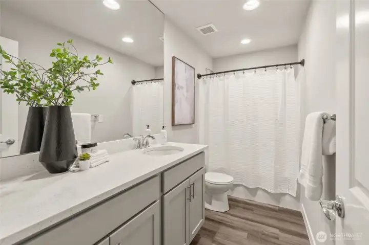 A bright, beautifully finished full bath featuring an expansive vanity, quartz countertop, and generous storage.