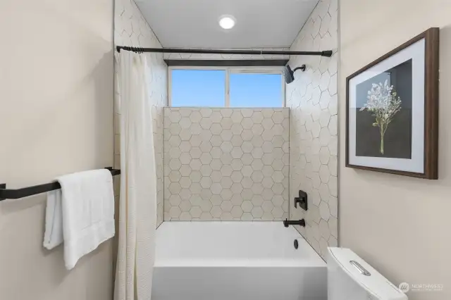 This shower is a statement piece, with crisp hex tilework, matte black accents, and a bright window bringing in natural light.