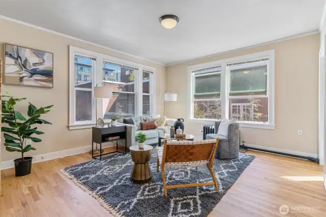 Spacious living room with oversized windows, natural light, and refinished original hardwood floors.
