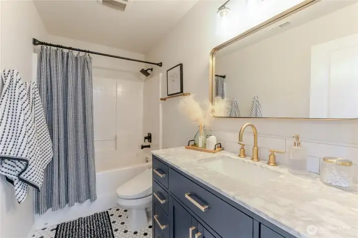 Remodeled hallway bath blends modern elegance with practical design, featuring navy cabinetry, granite counters, and brass accents for a crisp, elevated finish