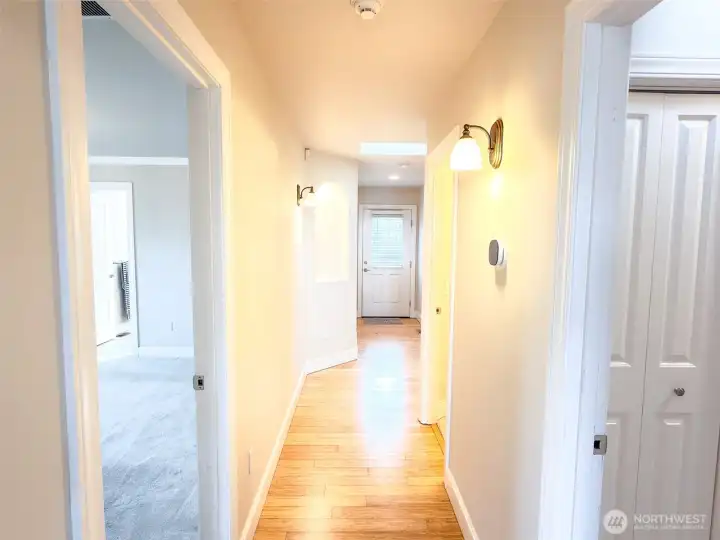 Hallway from great room: L to R; doorway to the Primary bedroom, with ensuite full bathroom, conveniently located closest to the great room.  Further down hallway, L to R is an art niche, the back door, hallway to the other 2 bedrooms, full bath, additional closets, doorway to the 1/2 bath and closest doorway on the right leads to the utility room and garage.