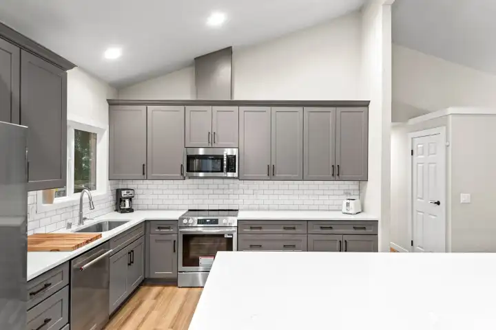 The kitchen features quartz countertops, nearly new stainless-steel appliances (2025), a classic white tile backsplash, and a large window with a serene, tree-lined outlook.