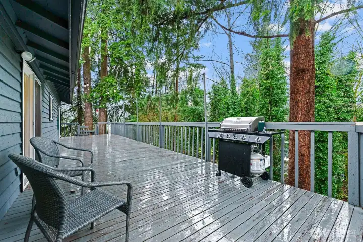 Another view of the expansive upper deck showcases the serene, treed outlook, with stairs in the background leading down to the lower deck.  Note-All Decks, Railings, and Stairs in front and back were just painted in February 2026.