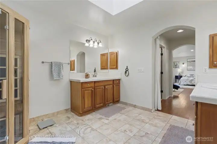 Primary ensuite bath view towards bedroom, his and her closets in the hall. Separate double vanities is a real convenience and I love the tile flooring and skylight!