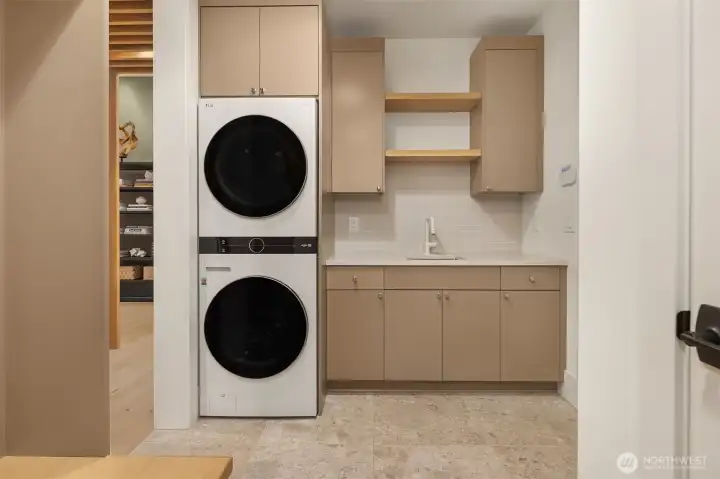 A third set of washer and dryer — this one on the main floor, tucked behind cabinetry with a dedicated sink and open shelving. The kind of detail that sounds like a luxury until you're actually living here.