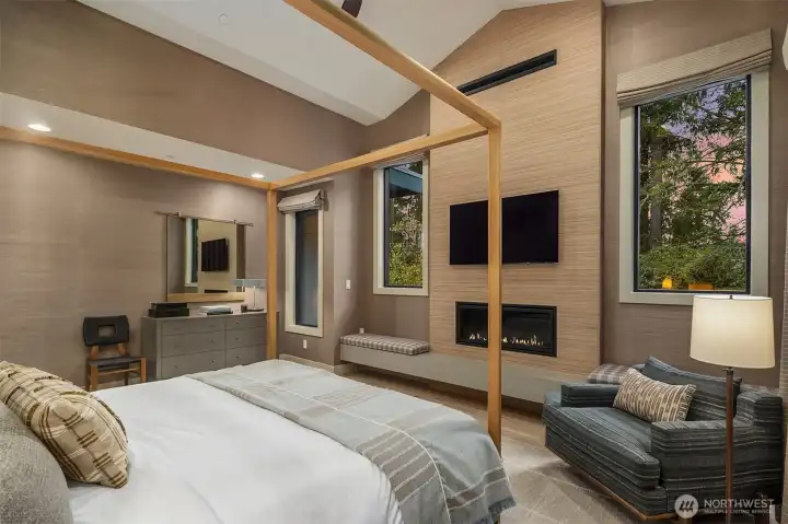 Thibaut Shang Extra Fine Sisal walls, a linear gas fireplace, motorized linen drapery, and treetop views at dusk. The primary suite that makes it genuinely hard to get out of bed in the morning.