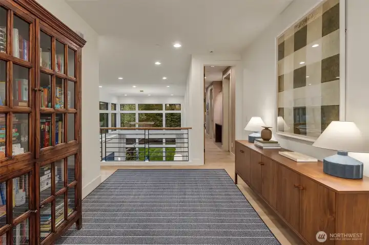 A wide-plank upper landing with steel railings, tree views, and the kind of thoughtful detailing that makes a hallway feel like part of the home — not just the space between rooms.