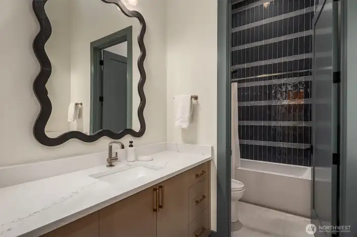 A sculptural mirror, deep navy vertical tile, quartz countertop, and heated floors.
