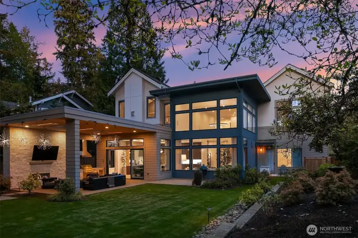 Soaring two-story window wall, cedar-clad terrace, and a glowing interior visible through every pane. The kind of exterior that stops you before you've even walked inside.