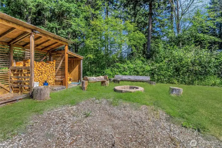 Outdoor gathering space with fire pit, adjacent covered woodshed for convenient firewood storage. Grass digitally enhanced.