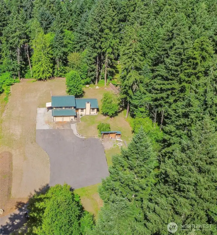 Additional aerial perspective showcasing the 1.22-acre private setting, offering ample usable space, abundant parking, RV potential, and room for a future shop surrounded by a peaceful, wooded backdrop.