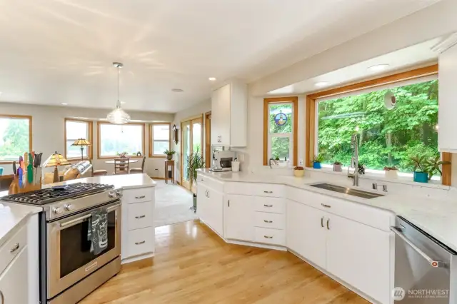 Features high-end stainless steel appliances, including a prominent gas range, set against sleek white cabinetry and expansive quartz countertops, offering ample prep space.