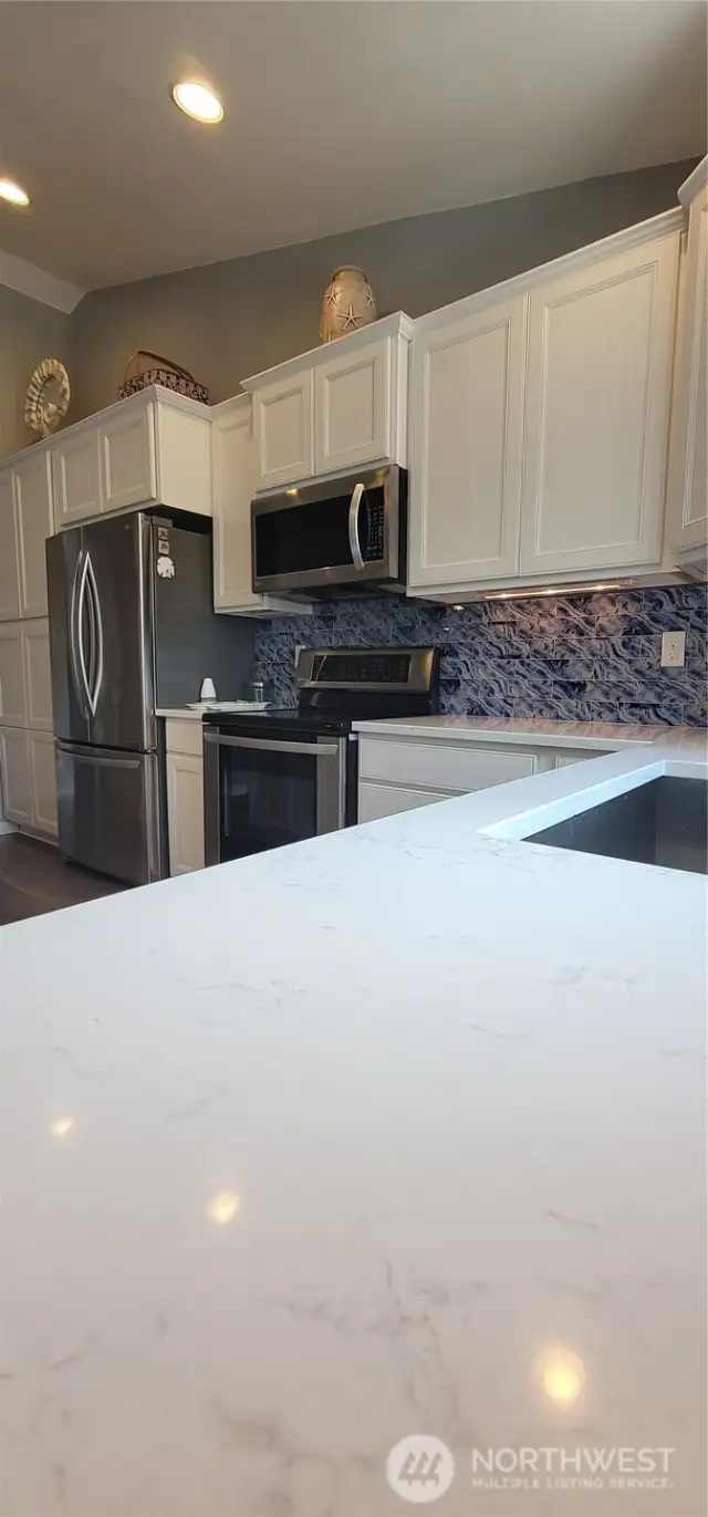 Light, bright, and beautifully designed, this canal-side kitchen is a coastal dream—featuring white cabinetry, gleaming appliances, and an elegant quartz countertop. The patterned blue-and-white glass backsplash adds a splash of charm, while modern finishes make every meal feel like a seaside occasion.