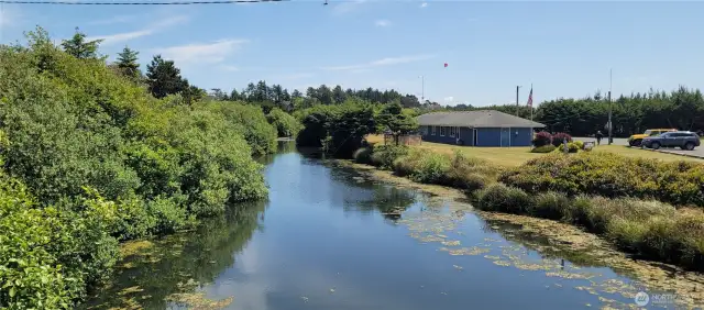 From the Surfside community bridge, enjoy a postcard-worthy view back toward your tranquil canal-front home—nestled among vibrant greenery with a clear path leading to the water’s edge. This serene vantage captures the essence of coastal living, where peaceful reflections and paddling adventures are just steps away.