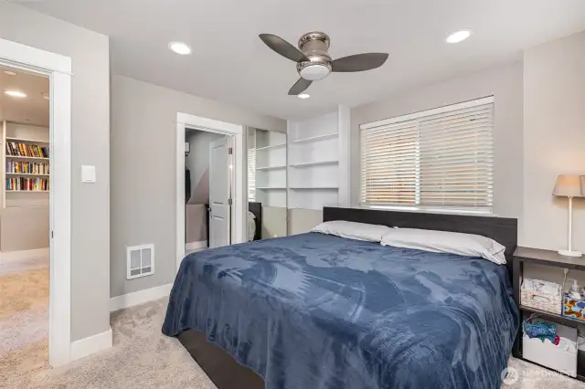 Welcome to the downstairs primary bedroom, complete with built-in shelving, a ceiling fan, spacious walk-in closet, and a private en-suite bathroom.