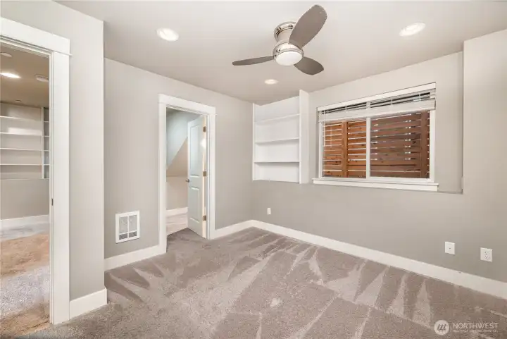Welcome to the downstairs primary bedroom, complete with built-in shelving, a ceiling fan, spacious walk-in closet, and a private en-suite bathroom.