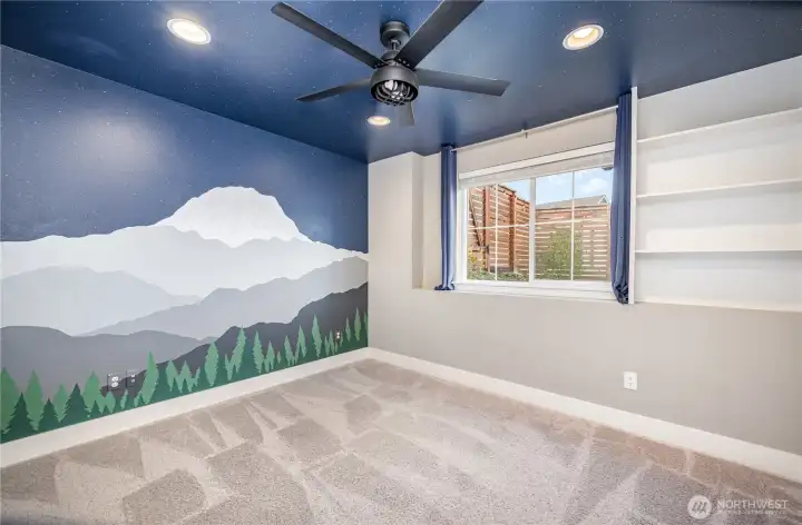 Charming downstairs guest bedroom showcases a custom mountain mural, ceiling fan, recessed lighting, and built-in shelving—perfect blend of style and function.